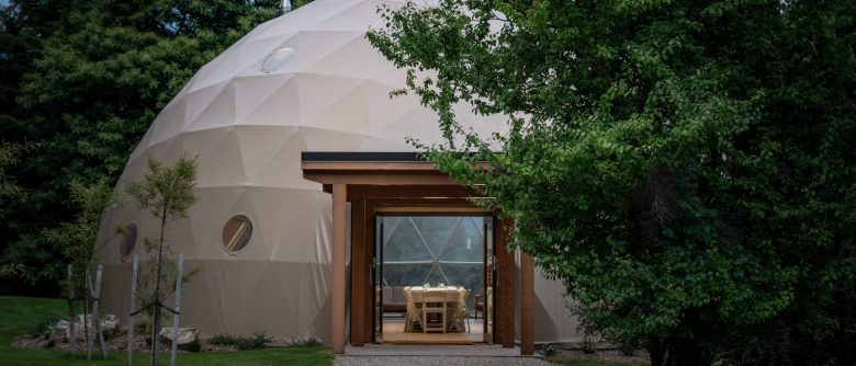 Close-up of the dome's exterior, with a view through the canopy entrance designed by Sorted Architecture, revealing tables elegantly arranged for an event.
