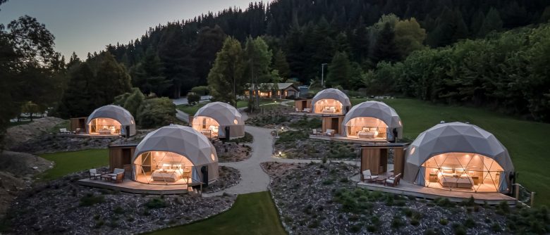 View of the glamping geodesic domes at dusk, softly lit, blending into the serene landscape with a warm, inviting glow.