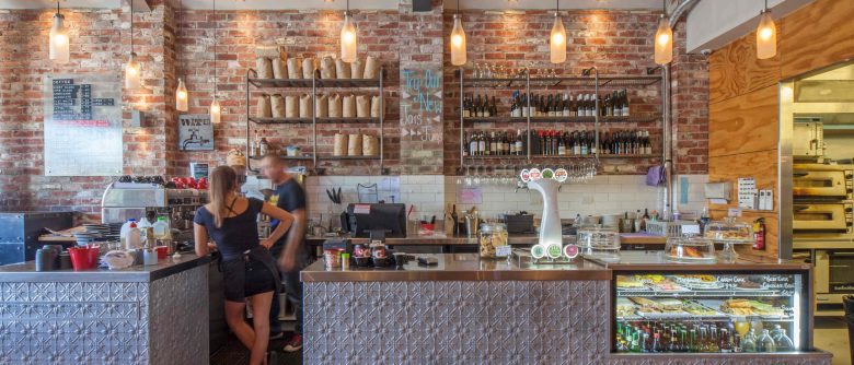 View of Urban Grind’s main bar and counter area, featuring warm brick and pressed panel finishes.