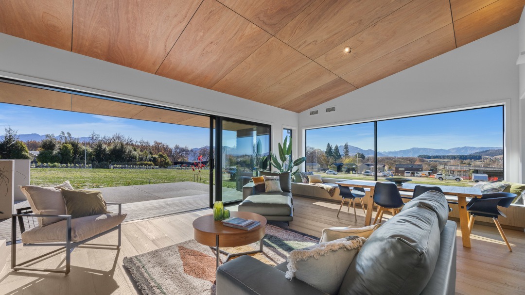 View across the living area showcasing open-plan design, comfortable furnishings, natural light, and a strong connection to the outdoor deck and landscape.