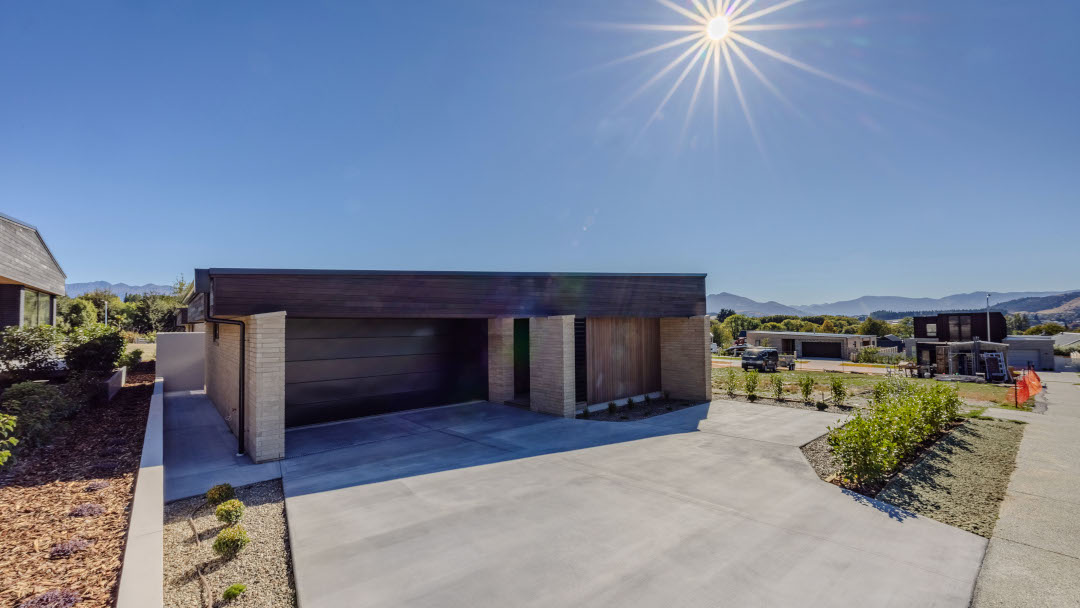 Sunlight shining over the garage, driveway, and entry of a contemporary architecturally designed three-bedroom home.