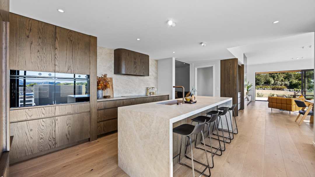 View across the kitchen island to the media room and private master suite entry, with large sliding glass doors opening to the outdoor patio.