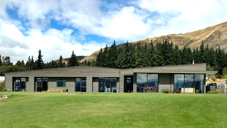 Front view of the house set against hills in the background, overlooking a green grass park.