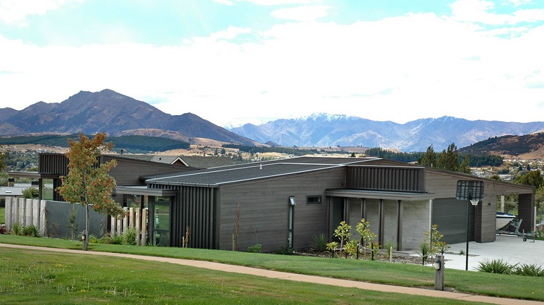 Looking across a park to the house entry and garaging showcasing exterior cladding of horizontal cedar weatherboards and board form tilt slab concrete