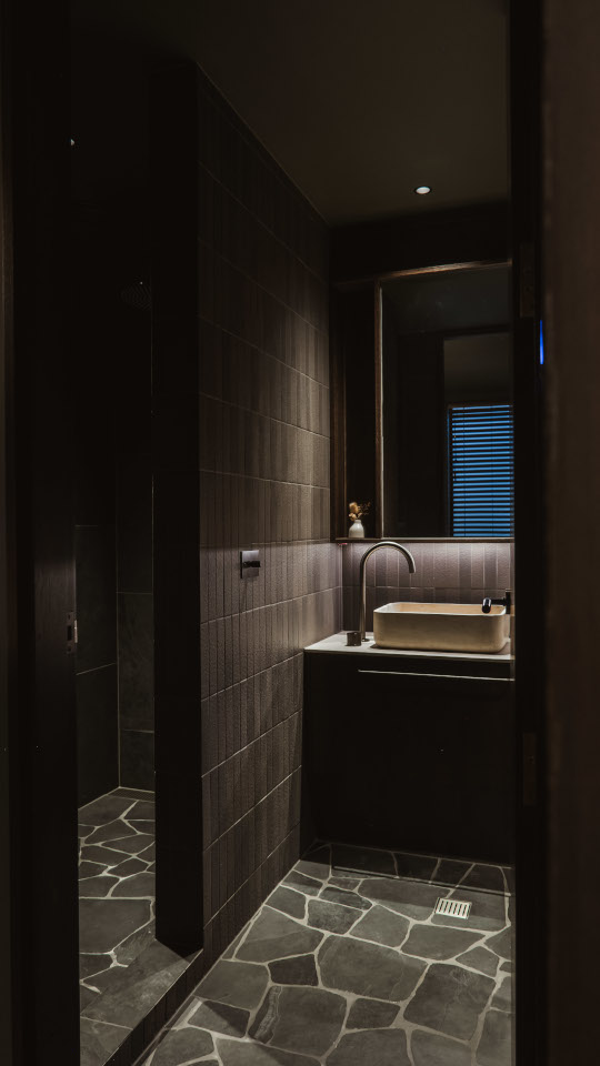 Contemporary bathroom with dark tiles and a stone floor, featuring a refined, luxury design and modern finishes