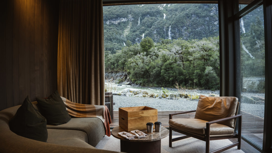 Lounge area of a luxury chalet, featuring warm timber interiors, large glass windows and a refined, contemporary alpine design.