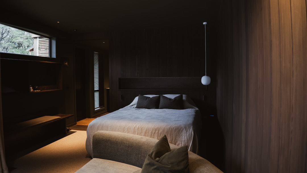 Bedroom of a luxury chalet lined with warm, dark timber, creating a rich and intimate interior atmosphere.