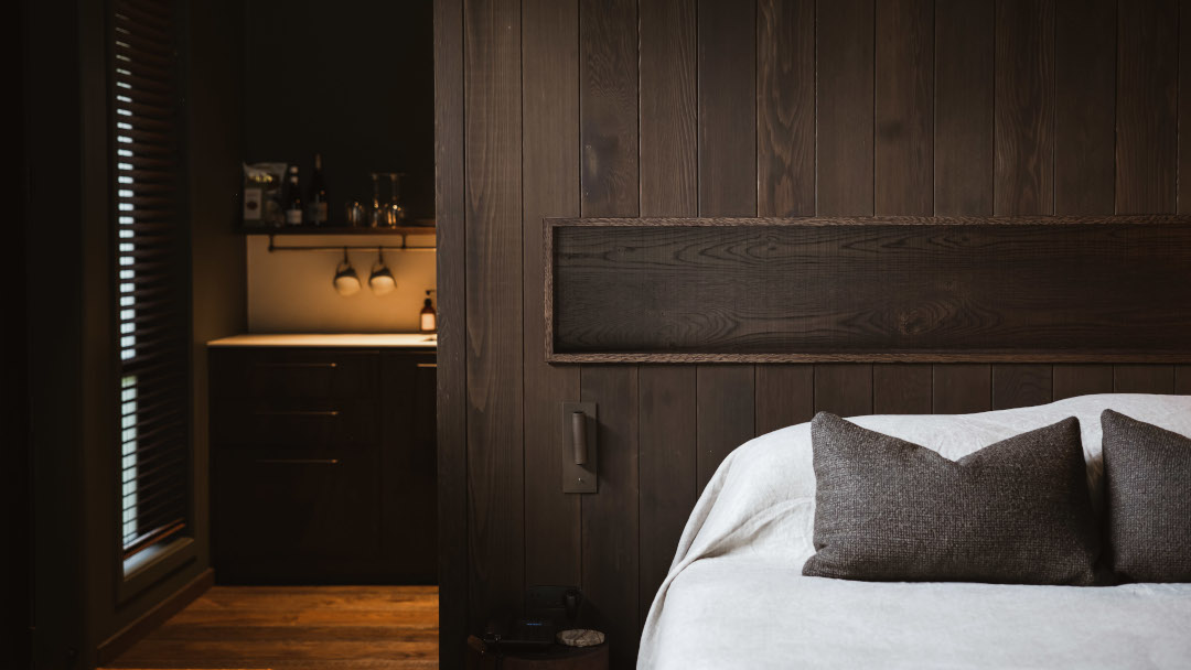 Looking through the wood-panelled bedroom toward the kitchen of a luxury chalet, featuring warm timber interiors and contemporary design.